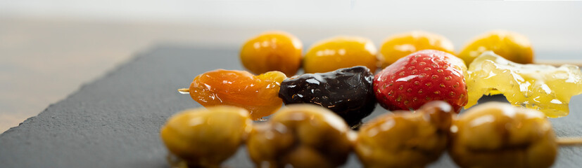 Caramelized fruit, street food. Tanghulu, fruit skewers covered with caramelized sugar. Dessert with: strawberry, dried fruit, chestnuts and kumquat. Web banner.