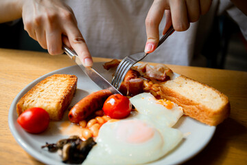 a girl with a knife and fork eats an English breakfast fresh tomatoes scrambled eggs fried eggs with rye white fresh bread and meat sausage pork sausage meat food tomorrow lunch meal health