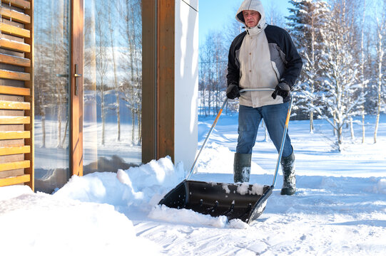 A man in winter clothes with a snow shovel cleaning the snow from the terrace of the house