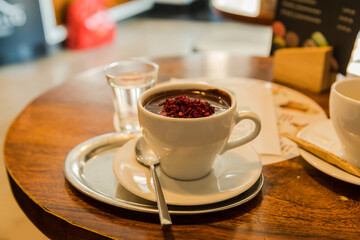A cup of hot chocolate, a teaspoon, a glass of clean water, on a wooden table in the restaurant....