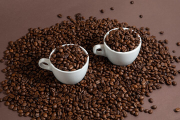 two cups of coffee on a pile of coffee beans on a brown background.