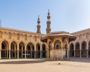 Ablution fountain mediating the courtyard of public historic mosque of Sultan al Muayyad, with background of arched corridors surrounding the courtyard, and minarets of the mosque, Cairo, Egypt