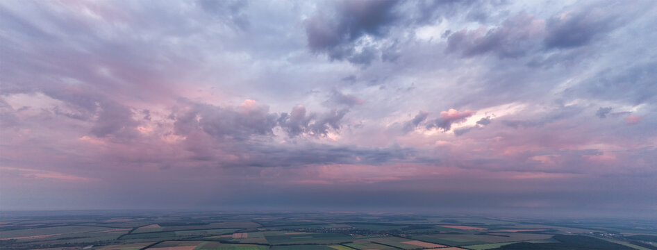 Panorama of pink sky with clouds over green land and fields. © malshak_off