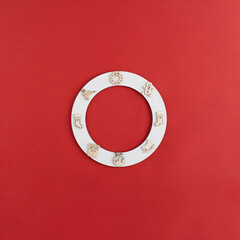 Naklejka premium New year white ring flat lay with wooden decoration baubles, reindeer, sock, a gift, cavalry and gingerbread man on red background. Creative Christmas minimal copy space concept.