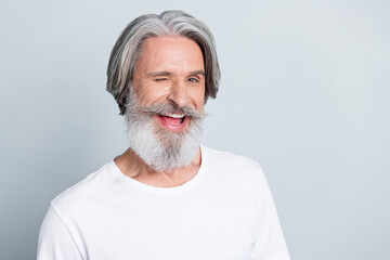 Photo of positive funky retired man wear white t-shirt smiling winking empty space isolated grey...