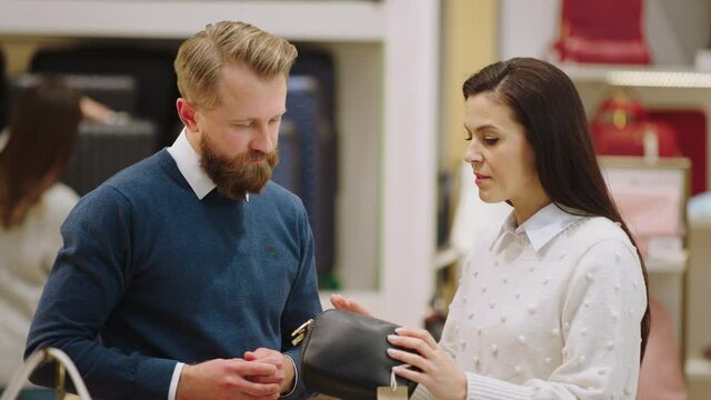Handsome customer man wants to buy a wallet he discussing with the saleswoman to decide what wallet are better