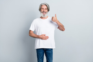 Portrait of attractive cheerful gray-haired man touching belly showing thumbup isolated over grey...