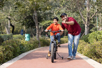 Cheerful father teaching son riding bicycle while admiring view at park.
