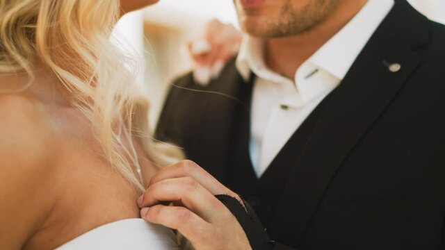 Gentle groom in black suit strokes chest of beloved young woman with blonde curly hair standing in street on sunny day closeup slow motion