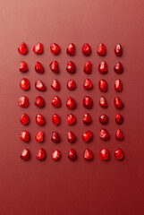 fruit background - pomegranate seeds are laid out in symmetrical even rows on a red background with a gradient