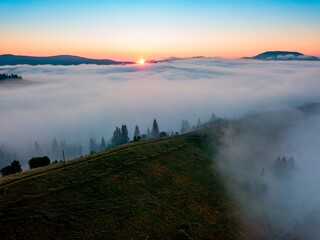 Obraz premium Fog spreads over the mountains at dawn. The sun rises on the horizon. Ukrainian Carpathians in the morning. Aerial drone view.