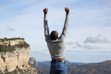 Excited man with black skin raising arms in nature