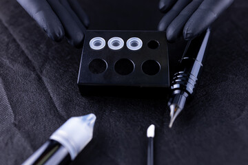 the hands of a permanent eyebrow makeup artist hold a stand on which white caps with tattoo pigment...