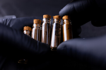 a master in black gloves holds bottles of henna for eyebrow coloring in front of him