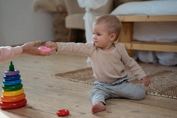Mother playing with her cute baby child pyramid game, giving toy sitting at home. Child development concept 