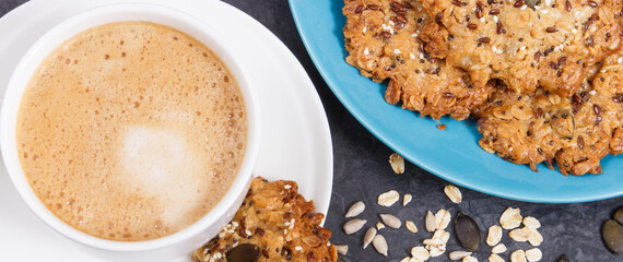 Cup of coffee with milk and fresh baked oatmeal cookies on blue plate. Delicious crunchy dessert
