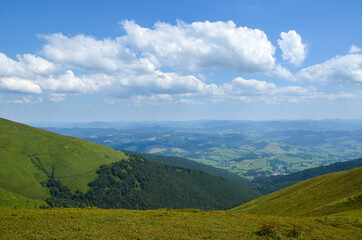 Naklejka premium Beautiful rural landscape from the mountain range to the valley with green hills, grassy meadow, forest and village on a sunny summer day. Carpathians, Ukraine