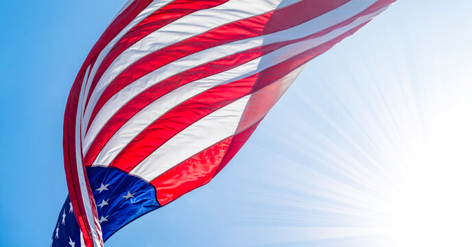 Low angle view of American flag waving in wind against clear sky with Sun