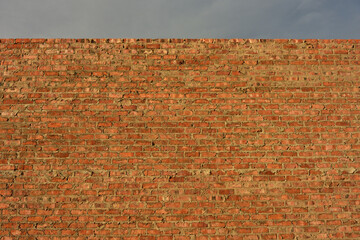 A newly built raw brick wall in golden sunlight against a grey sky