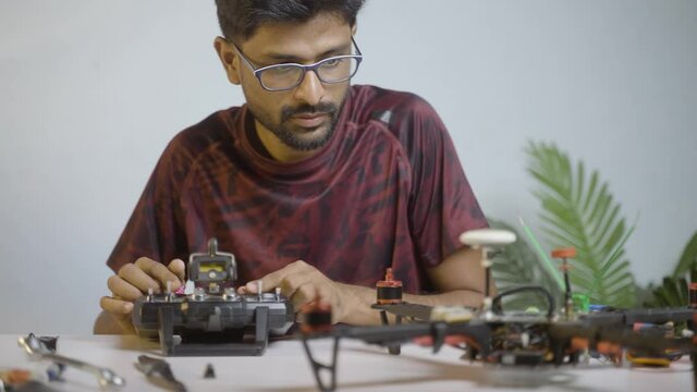 Young professional engineeer examining or testing drone configuration setting using remote control while repairning drone at shop - concept of uav or quad copter repair service and hobby