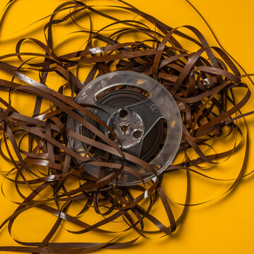 Overhead view of retro recording tape reel with unspooled&nbsp;tape&nbsp;against yellow background