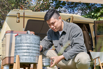 A young man pouring water from a drinking fountain in front of a camping car