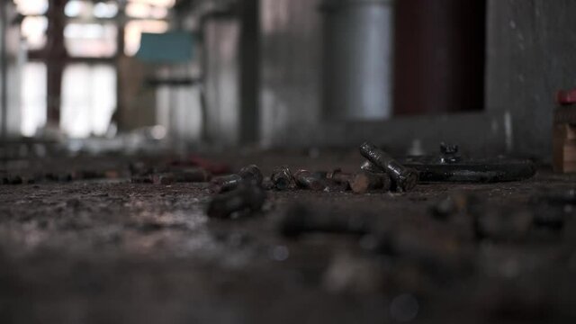 Rack focus rusty bolts lie on old, dirty floor in abandoned, broken factory. symbol of destruction of car factories in Detroit. People left building and did not clean up. wooden chair in background.
