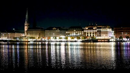 Hamburg, Germany. Townhall tower, buildings and Alster lakes at night. Cityscape. Reflection of lights in water. 