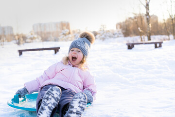 little girl rides down the slide on the ice, cheerful child, emotions from winter fun