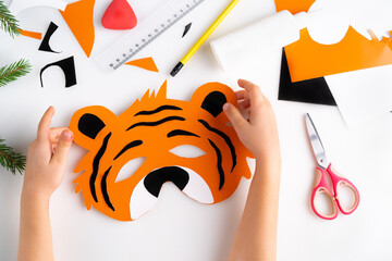 the process of making a children's New Year tiger mask with a child made of colored paper, top view, symbol 2022, step-by-step