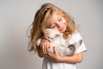 Fototapeta na wymiar a little blonde girl hugs a cute white kitten who licks her hand, a child and a kitten, a beautiful girl smiles