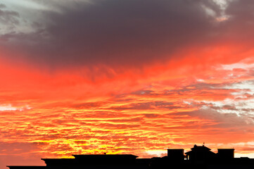 front view, far distance of a building  roof edge in silhouette, against a colorful low clouds, threatening rain at sunset