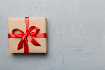 Holiday gift box wrapped in craft paper with colored bow on table background. Top view, flat lay, copy space