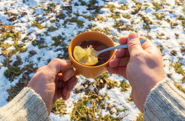 People hand hold an orange mug of hot herbal tea in cold winter. Prevention of viral diseases lemon...