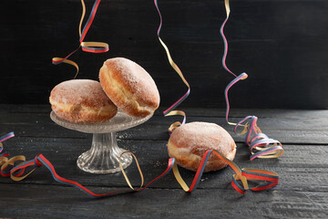 Berliner doughnuts or Krapfen with colorful party streamers on a dark rustic wooden table, traditional pastry for New Year or carnival, copy space, selected focus