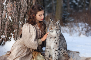 Beautiful girl in historical dress with lynx in winter forest. Fantasy portrait