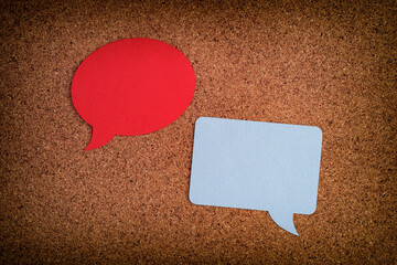 Two speech bubbles, one round, one square laying on a cork board
