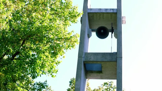 high bell tower of the chapel in the cemetery near the tree, a large heavy bell is ringing, the concept of a call to worship, wedding, funeral, funeral service, fire signal