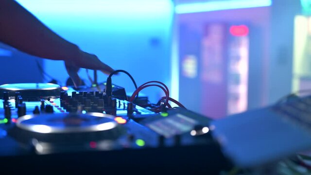 Tracking shot of a Man DJ playing with mixer and digital turntables. CDJ turntables with wires, button and sliders being played by electronic music Disc Jockey at nightclub. High quality 4k footage