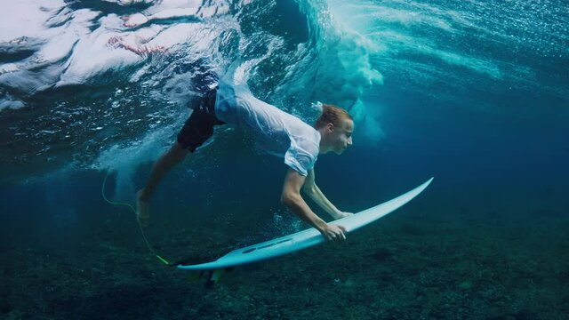 Teen boy dives underwater with surf board and confidently passes the wave