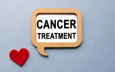 The inscription CANCER TREATMENT on a wooden template, against the background of scattered a red heart. Medical concept.