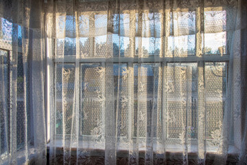 The window in the terrace is covered with a calico white curtain. Rural terrace. Evening light.