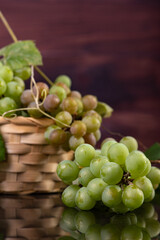 Grapes, bunches of green grapes placed together with a straw basket on reflective surface, selective focus.
