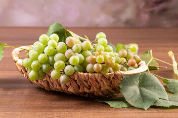 Grapes, bunches of green grapes placed together with a straw basket on wooden surface, selective focus.