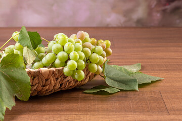 Grapes, bunches of green grapes placed together with a straw basket on wooden surface, selective focus.