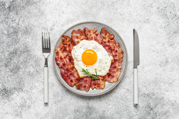 Fried egg with bacon on a plate, gray grunge background. Delicious appetizing breakfast. Top view, flat lay, copy space.