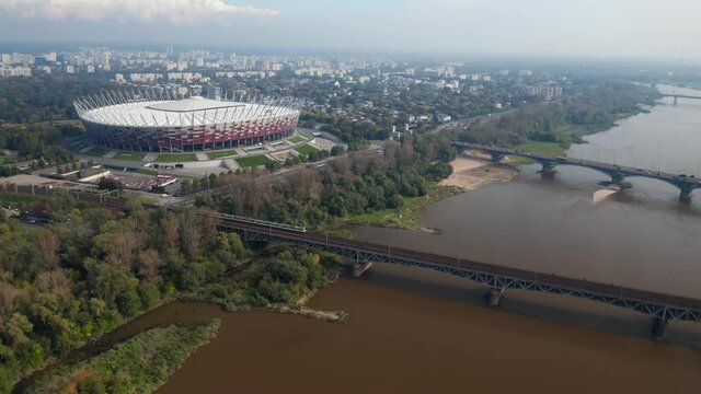 slide and pan footage of modern National stadium on Vistula riverbank. Train riding on bridge over water. Warsaw, Poland