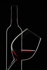Glass and bottle of red wine on a black background.