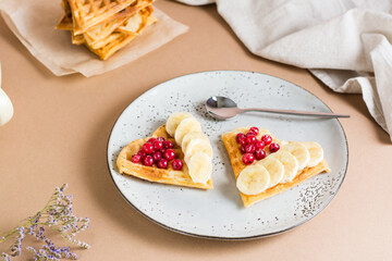 Heart shaped Belgian waffles with red berry and banana on a plate and a stack of waffles on the table. Valentine's Day