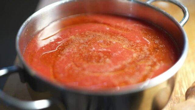 Looked down shot of cook or chef spreads and adds salt to a tomato sauce or ketchup boiling in a steel pan. Vegetarian ingredient for a traditional Italian meal.